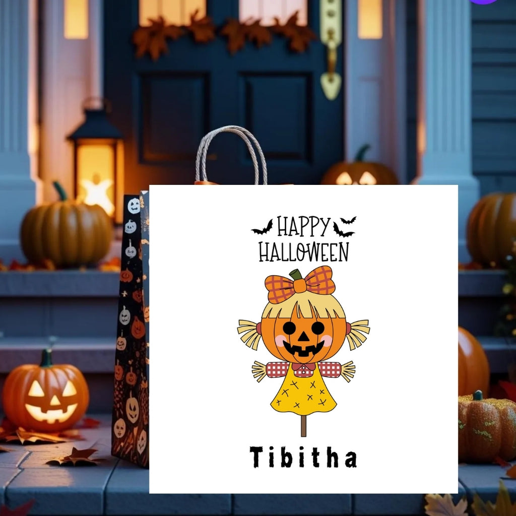 A white Halloween gift bag with gray rope handles, featuring a cartoon jack-o'-lantern character and the text 'Happy Halloween' and 'Tibitha'. A second black bag with orange pumpkin illustrations stands behind it on a porch decorated with pumpkins and autumn leaves.