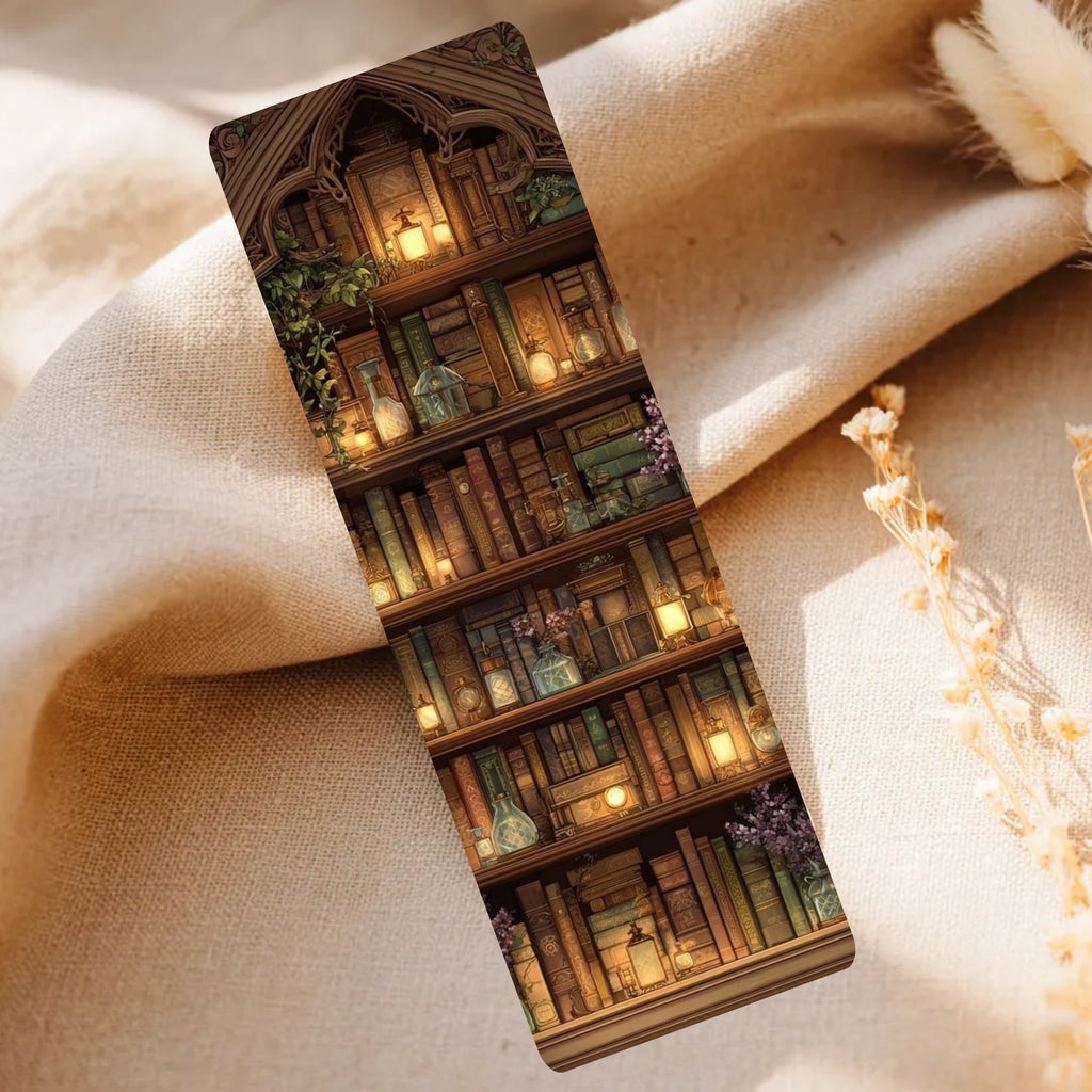 A slim rectangular bookmark or card featuring a printed illustration of a cozy library bookshelf with candles, books, and greenery, placed on draped beige fabric with dried flowers nearby.