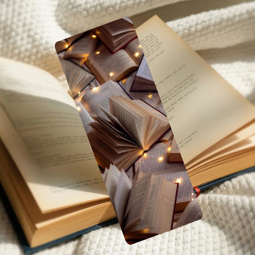 A rectangular bookmark or card featuring an artistic print of stacked open books with warm fairy lights, placed over an open book on a textured cream blanket.