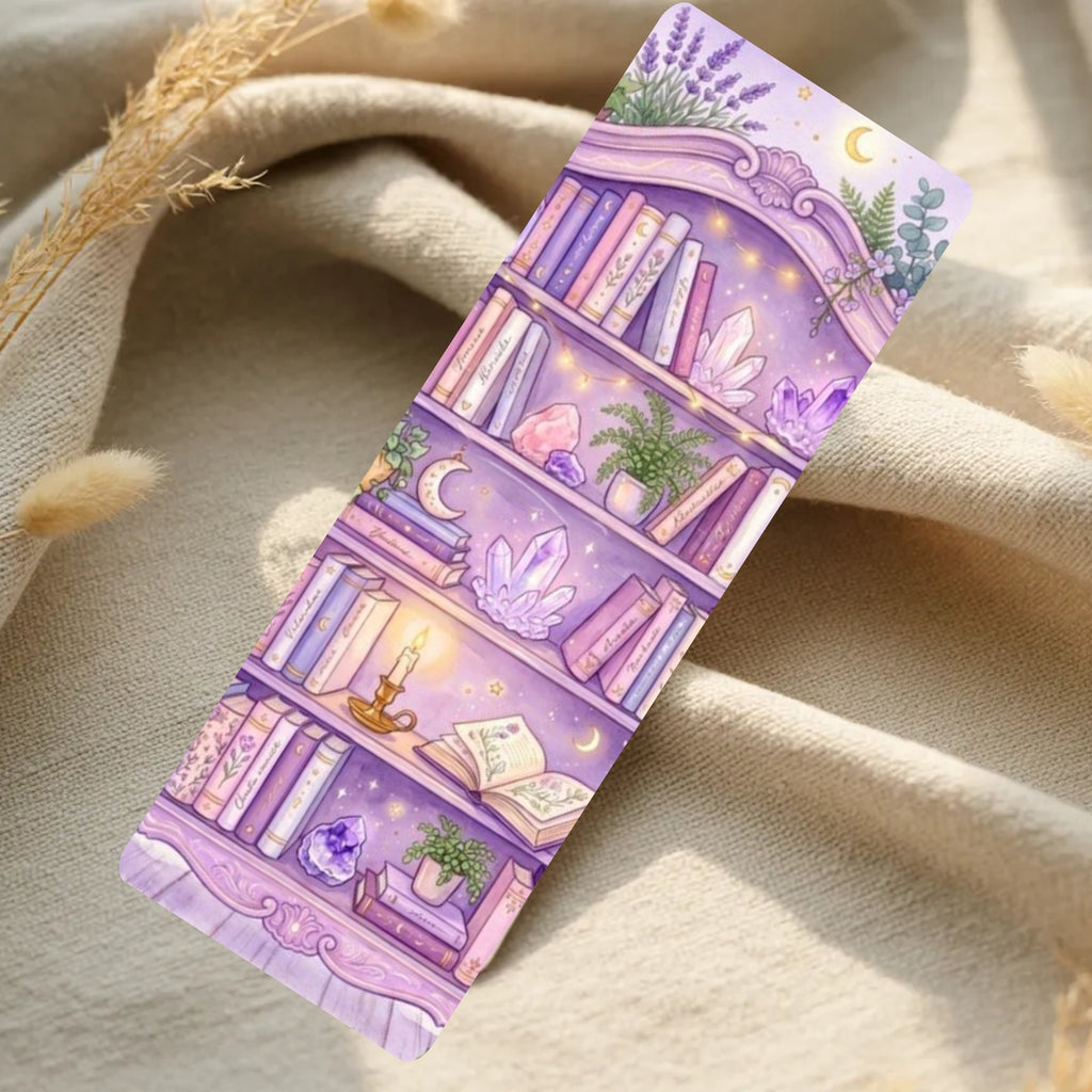 A long rectangular decorative item with a pastel purple illustration of a bookshelf, crystals, plants, candles, and moons, photographed on draped beige fabric with dried grass props.
