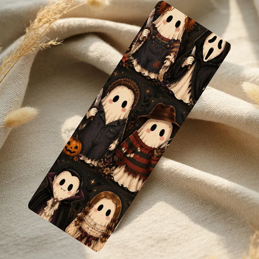 A slim rectangular phone case featuring a repeating Halloween ghost pattern, displayed diagonally on a soft beige fabric background with dried grass stems.