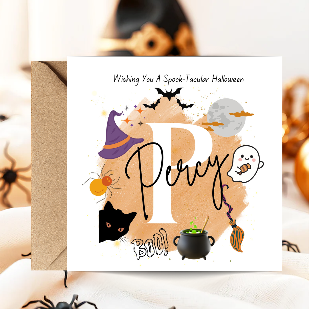 A square white greeting card with a kraft envelope, featuring Halloween-themed illustrations and the text 'Wishing You A Spook-tacular Halloween' and 'Percy BOO'. The card is displayed on a soft fabric surface with blurred spider decorations in the background.
