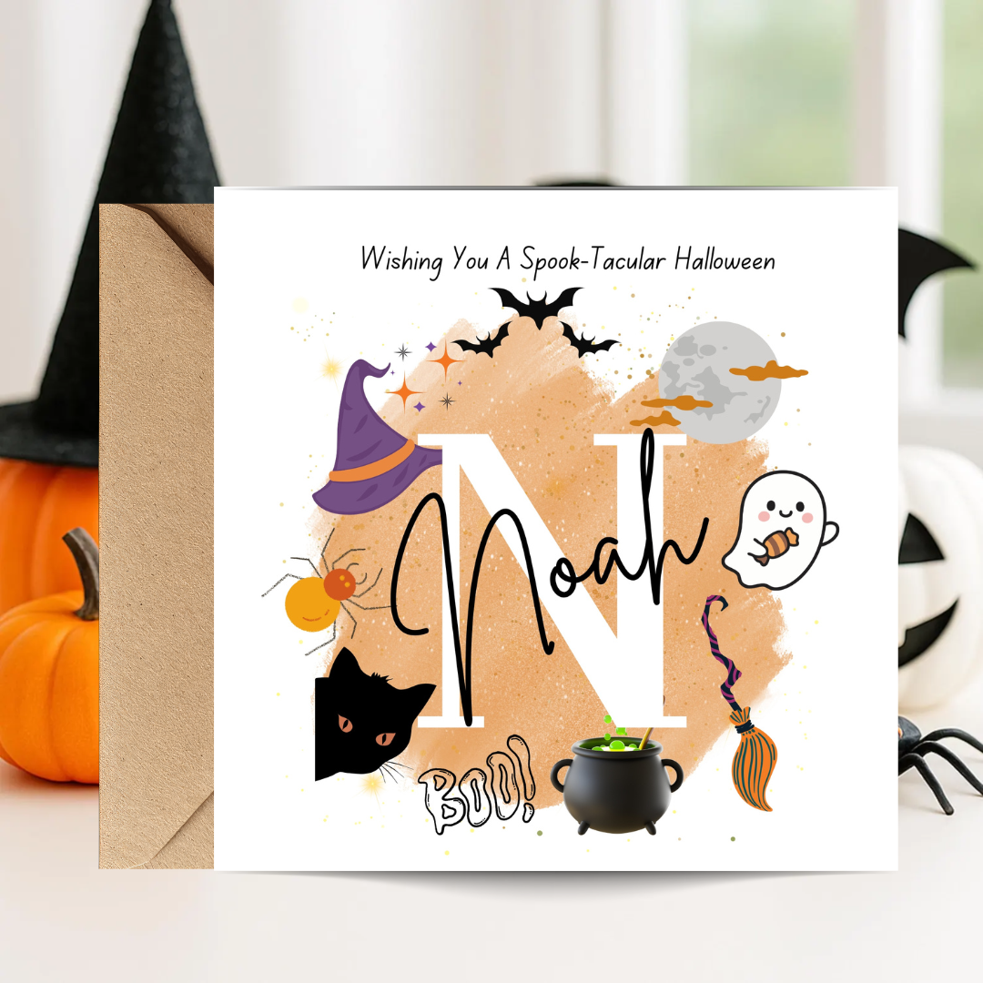 A square Halloween greeting card with a kraft envelope, displayed on a light surface with decorative pumpkins and a witch hat around it. The card features a large letter 'N' with the word 'Noah' written across it, plus spooky illustrations including bats, a ghost, a cauldron, a broom, a spider, a cat, and a moon, with the text 'Wishing You A Spook-Tacular Halloween' at the top.