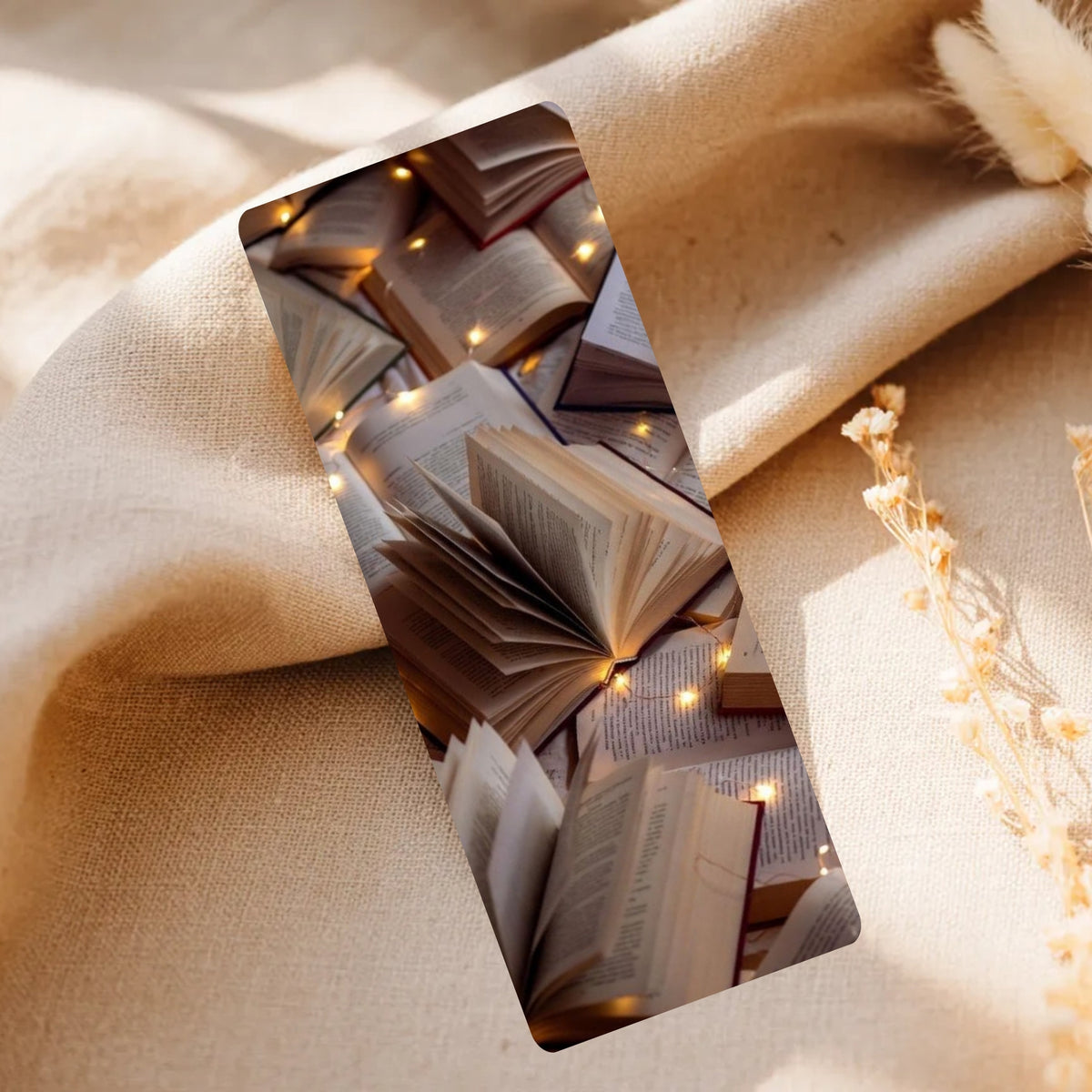 A rectangular phone case featuring a printed design of open books and warm fairy lights, styled on a beige linen fabric with dried flowers.