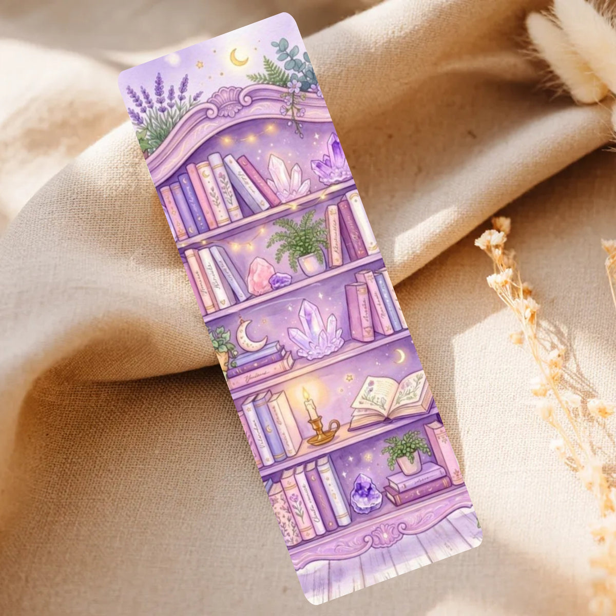 A lavender and purple bookmark featuring an illustrated whimsical bookshelf with books, crystals, candles, and plants, styled on a beige fabric background with dried flowers.